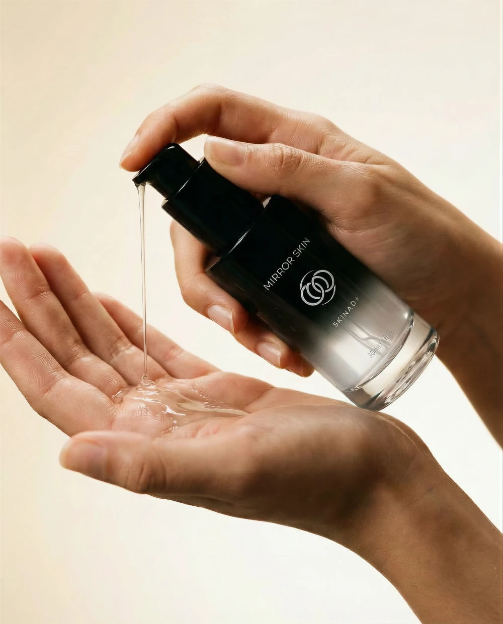Hand holding a skincare bottle with dropper over another hand on a neutral background